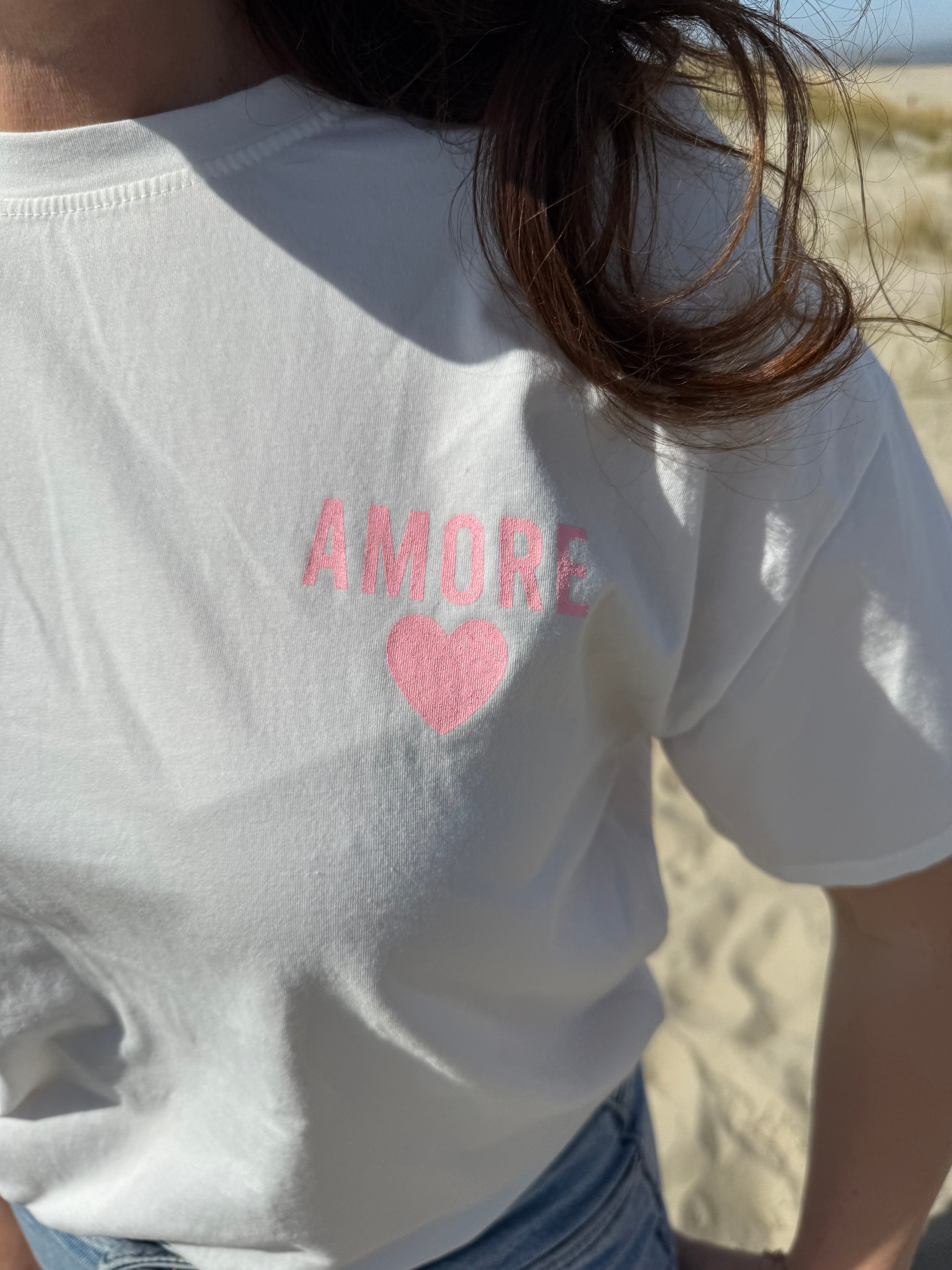 Oversize T-Shirt zum Verlieben. Kleines süßes Herz auf der Brust und ein großer Statement Print auf dem Rücken in rosa mit Amore. Das T-Shirt ist weiß.