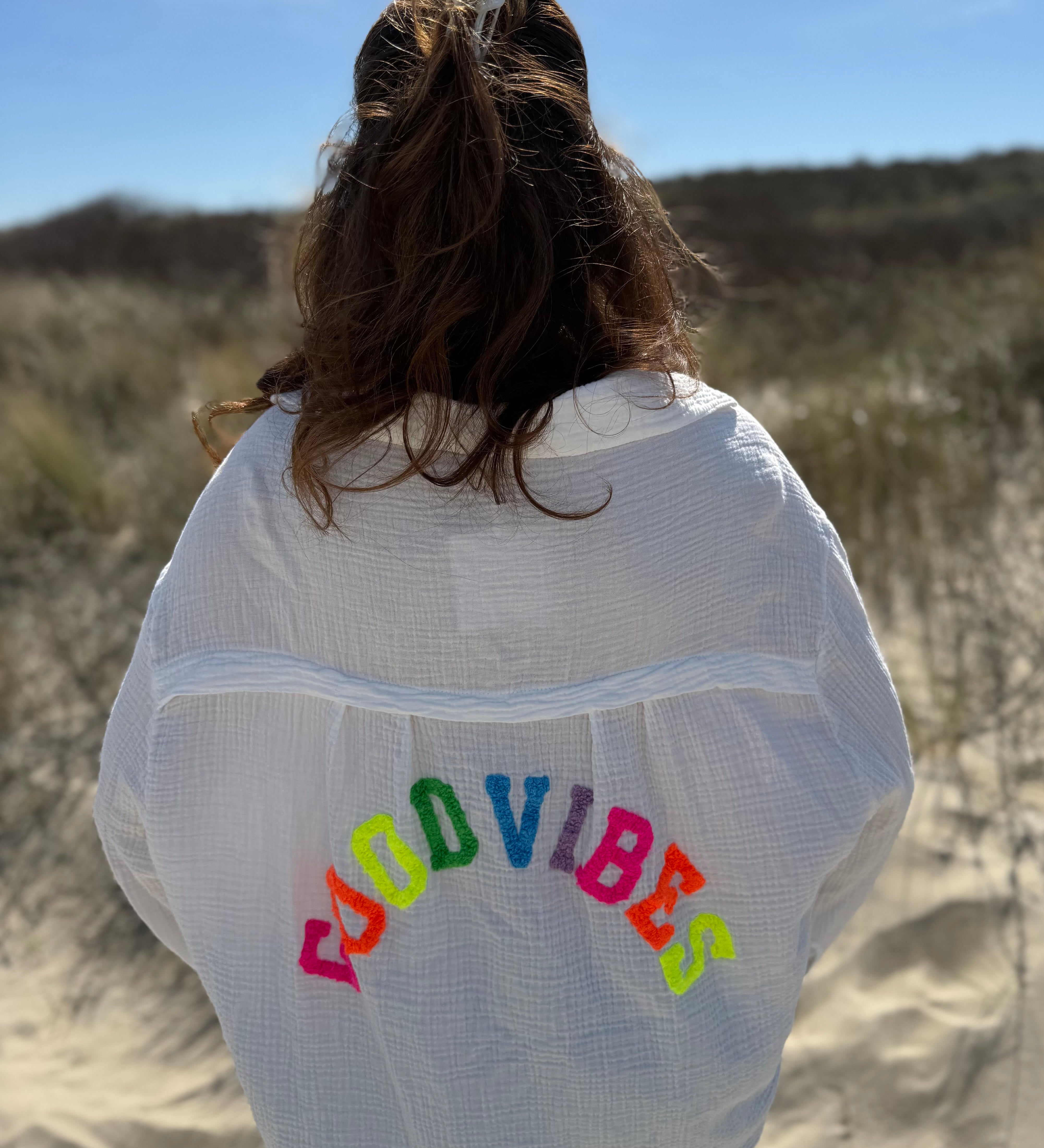 Musselinbluse im lockeren Oversize Look mit langen Ärmeln. Eyecatcher ist ein bunter GOOD VIBES Aufdruck am Rücken. Die Bluse ist weiß.