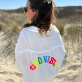 Musselinbluse im lockeren Oversize Look mit langen Ärmeln. Eyecatcher ist ein bunter GOOD VIBES Aufdruck am Rücken. Die Bluse ist weiß.