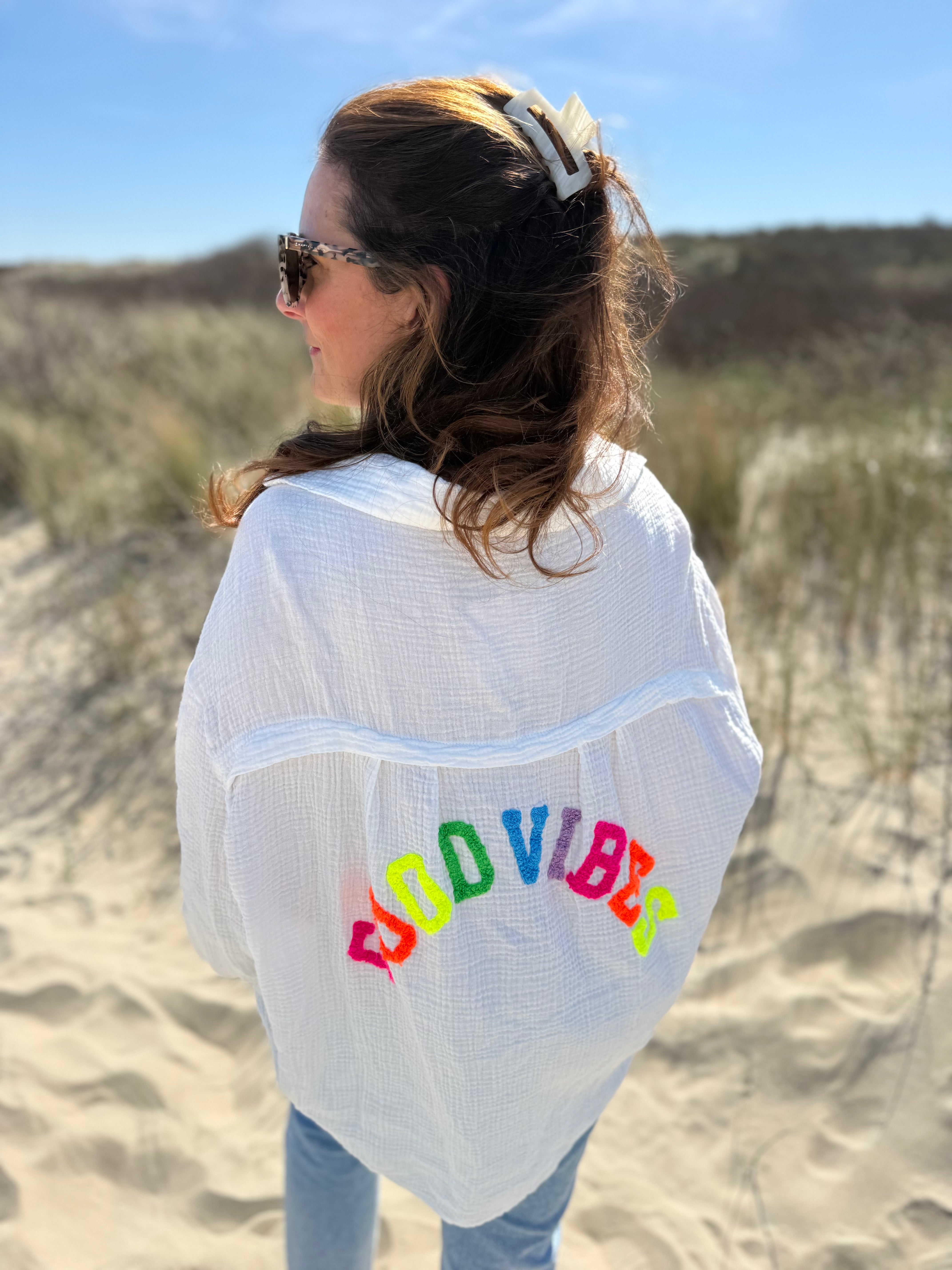 Musselinbluse im lockeren Oversize Look mit langen Ärmeln. Eyecatcher ist ein bunter GOOD VIBES Aufdruck am Rücken. Die Bluse ist weiß.