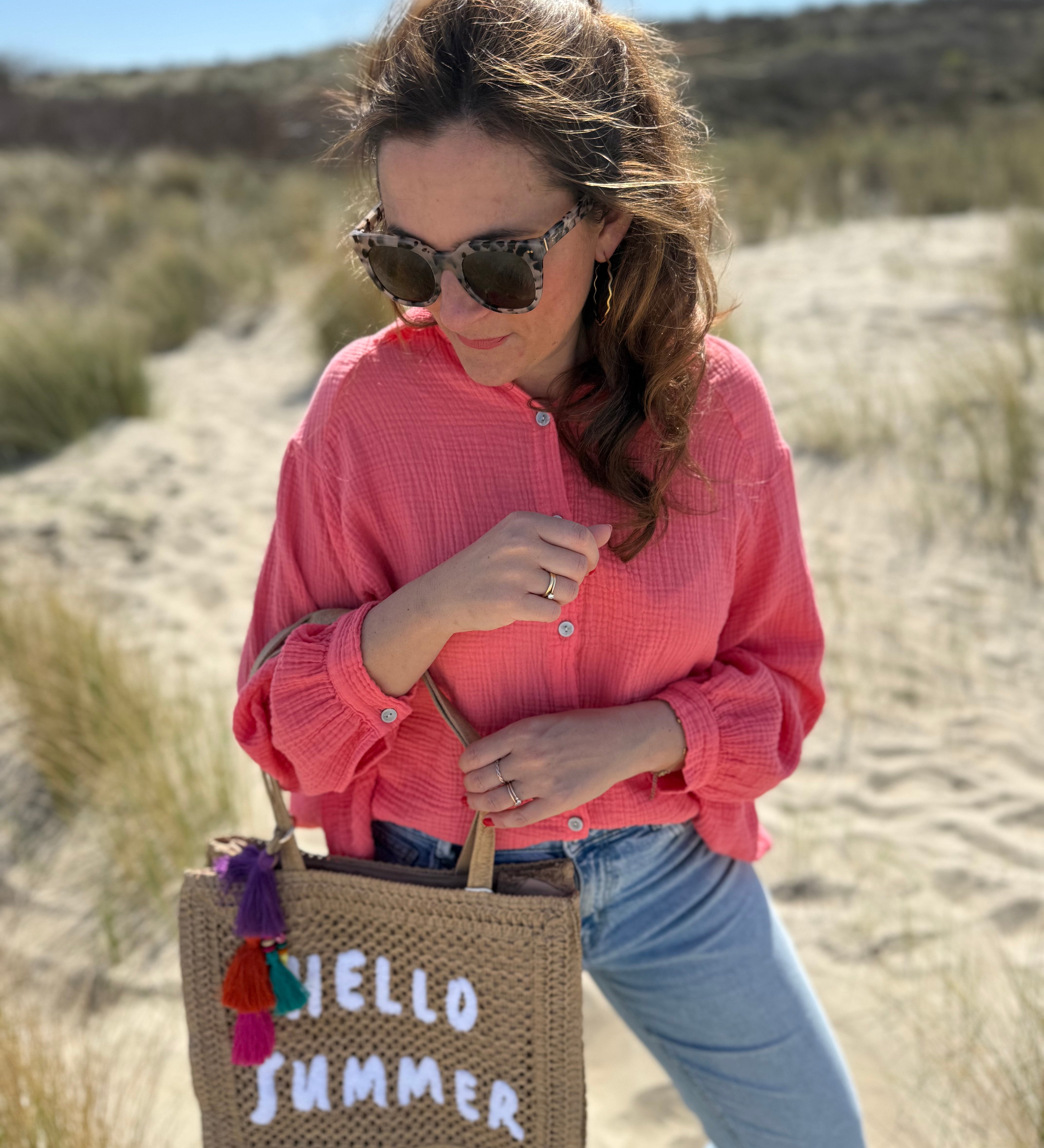 Tasche aus naturfarbenem Bast mit weißem HELLO SUMMER Aufdruck. An dem Henkel hängt ein Anhänger aus bunten Quasten im Boho Look