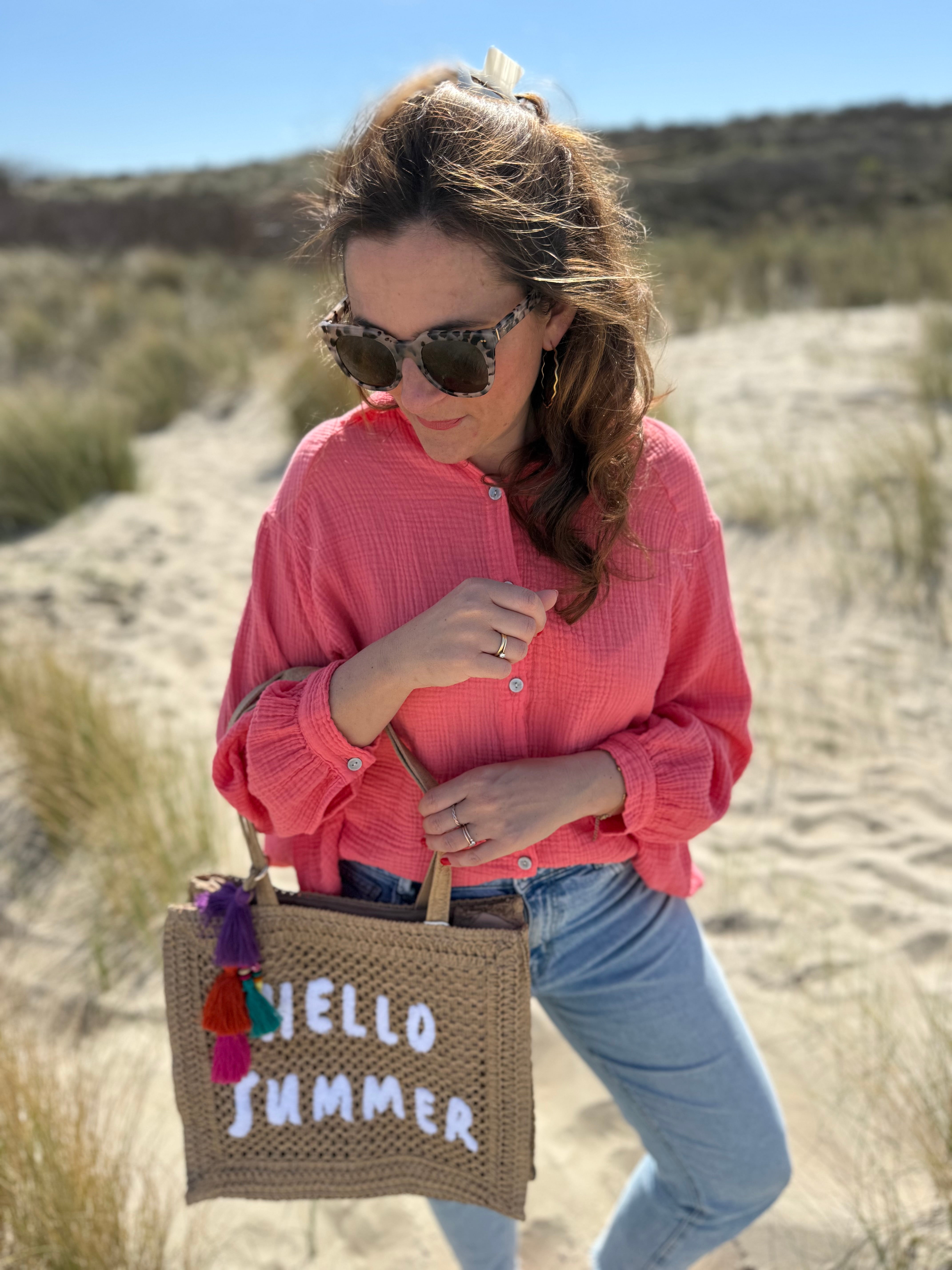 Tasche aus naturfarbenem Bast mit weißem HELLO SUMMER Aufdruck. An dem Henkel hängt ein Anhänger aus bunten Quasten im Boho Look