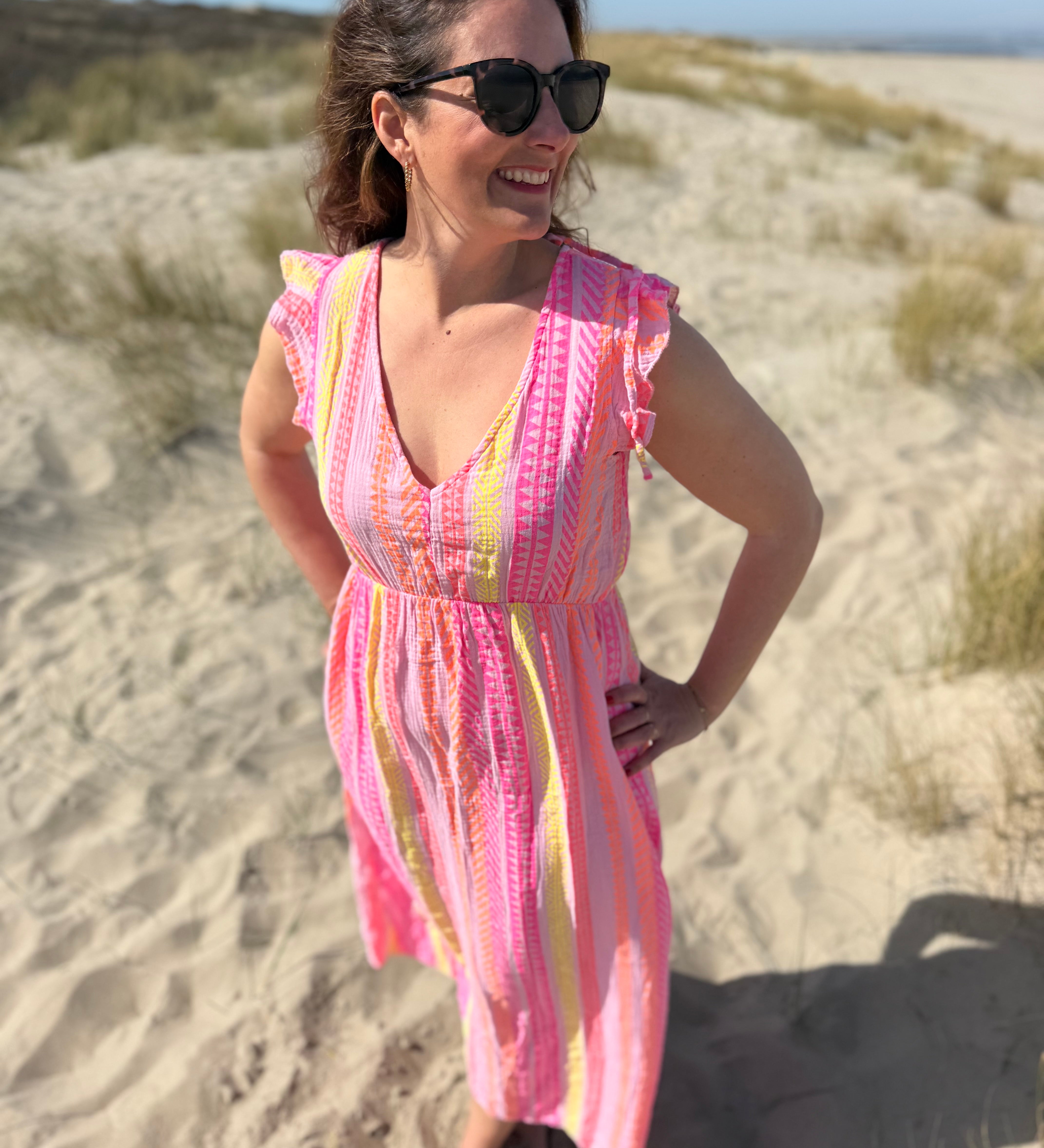 Musselinkleid in Maxilänge mit V Ausschnitt und kurzen Flügelärmeln. Das Kleid ist rosa mit pink, gelb und orangenen Ethno Muster.