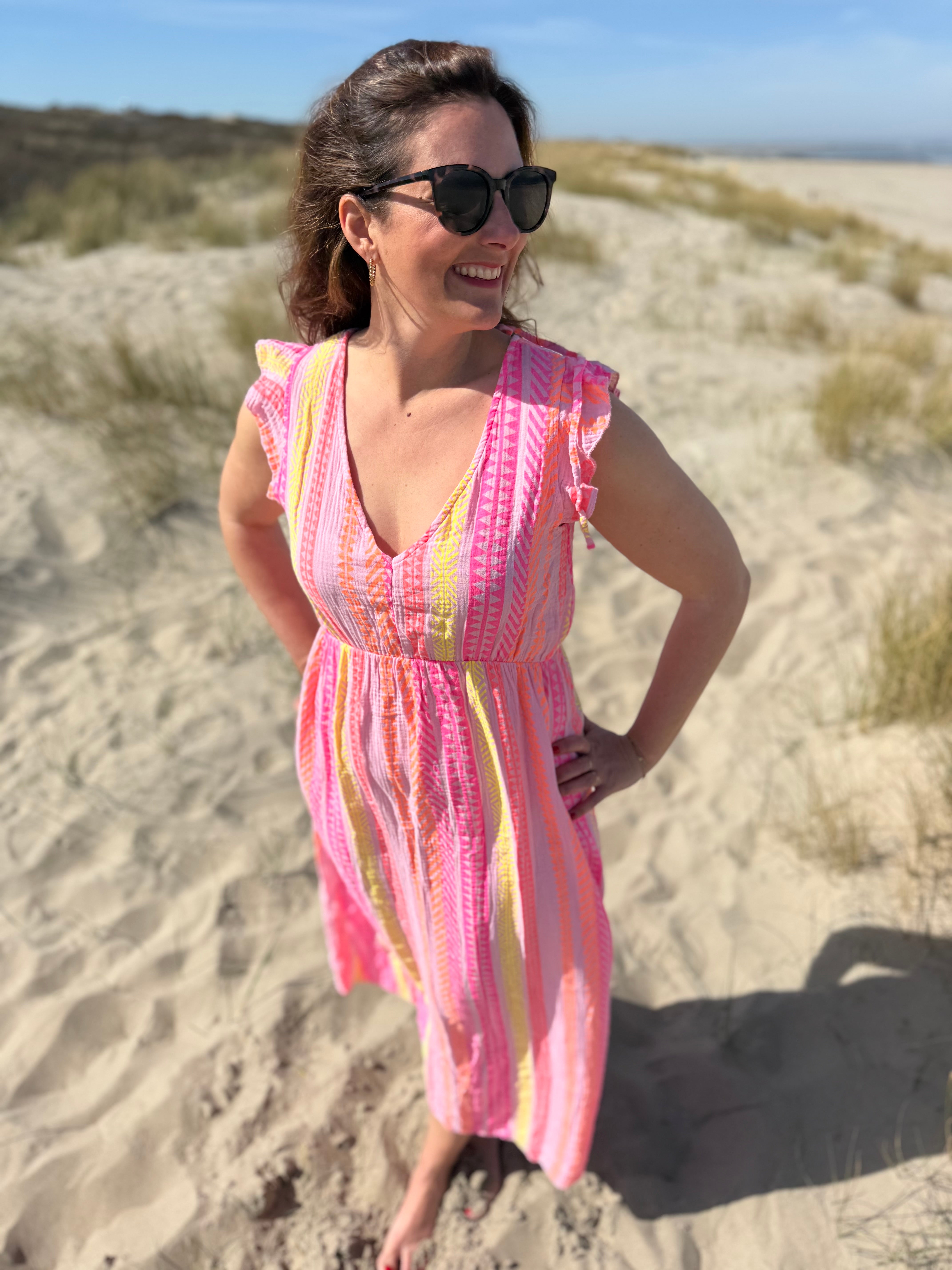 Musselinkleid in Maxilänge mit V Ausschnitt und kurzen Flügelärmeln. Das Kleid ist rosa mit pink, gelb und orangenen Ethno Muster.