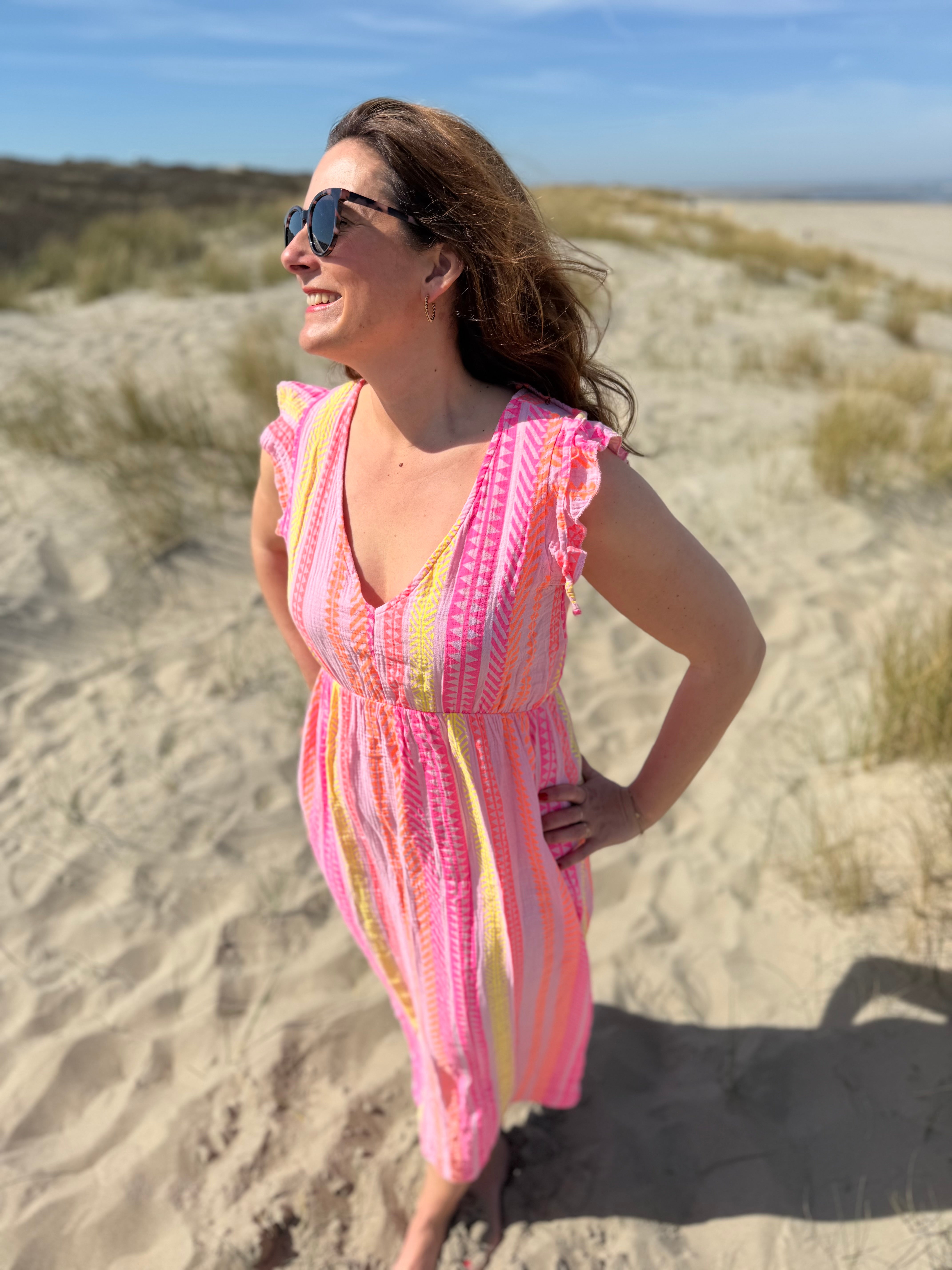 Musselinkleid in Maxilänge mit V Ausschnitt und kurzen Flügelärmeln. Das Kleid ist rosa mit pink, gelb und orangenen Ethno Muster.