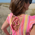 Musselinkleid in Maxilänge mit V Ausschnitt und kurzen Flügelärmeln. Das Kleid ist rosa mit pink, gelb und orangenen Ethno Muster.