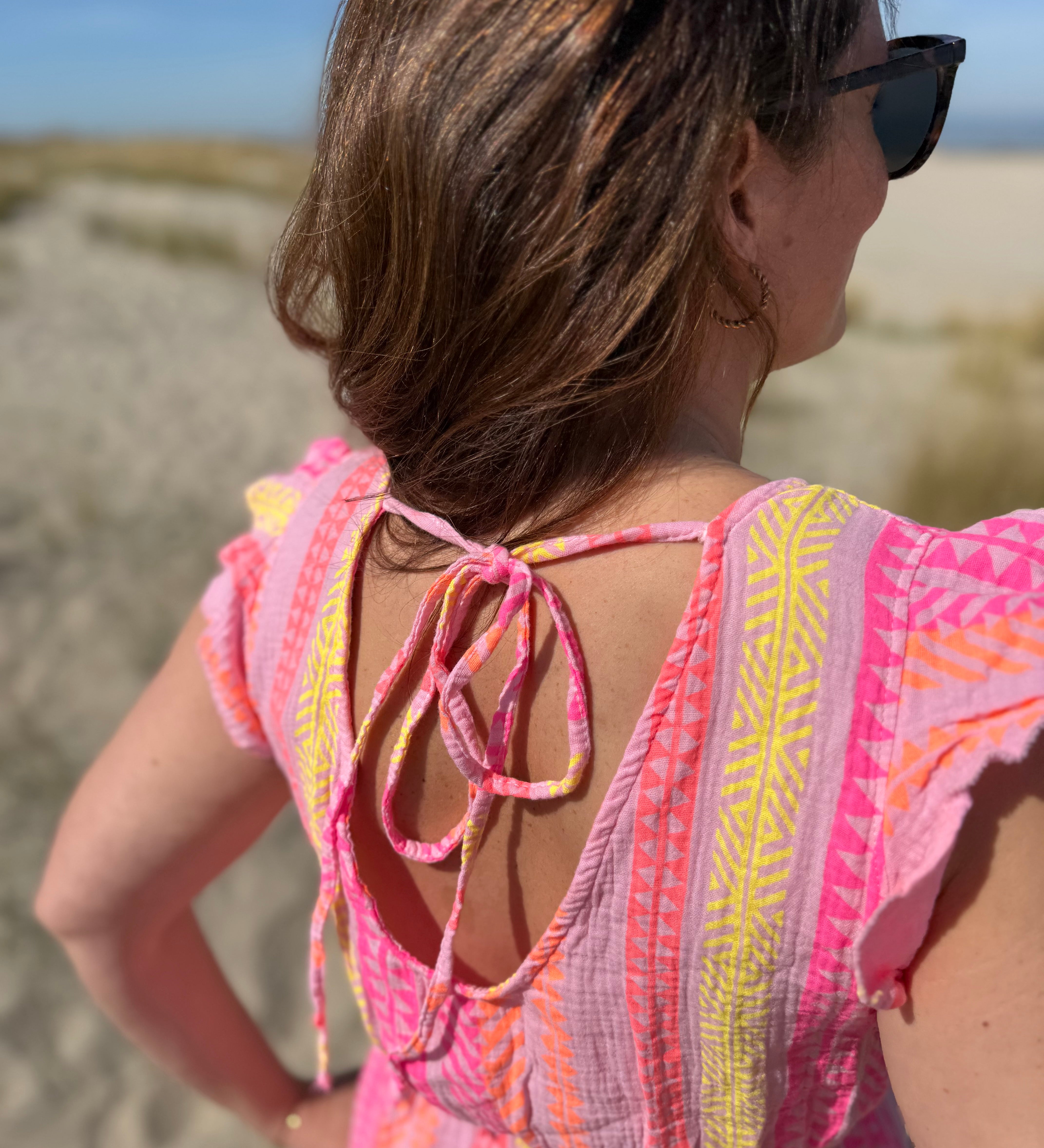 Musselinkleid in Maxilänge mit V Ausschnitt und kurzen Flügelärmeln. Das Kleid ist rosa mit pink, gelb und orangenen Ethno Muster.