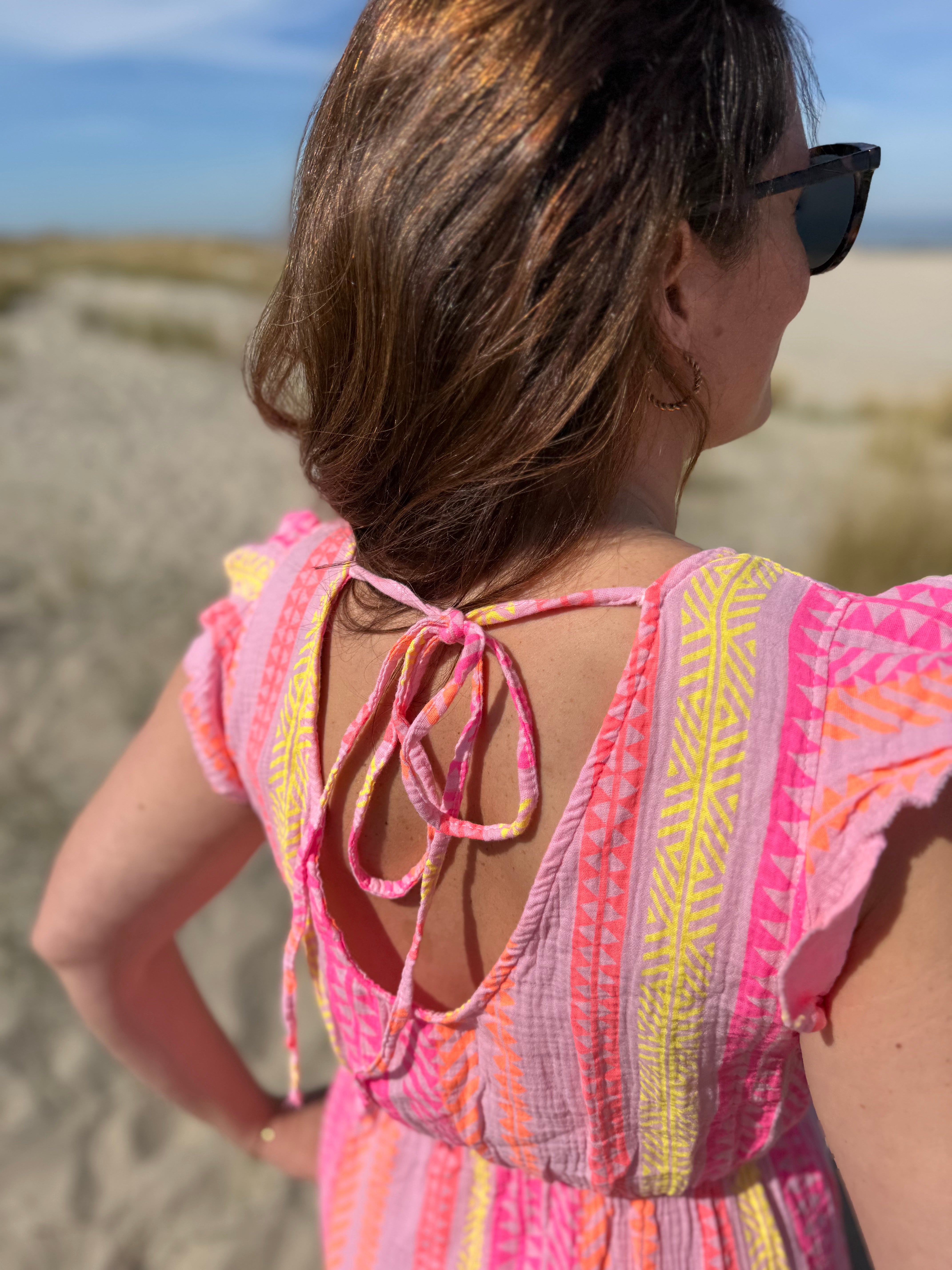 Musselinkleid in Maxilänge mit V Ausschnitt und kurzen Flügelärmeln. Das Kleid ist rosa mit pink, gelb und orangenen Ethno Muster.
