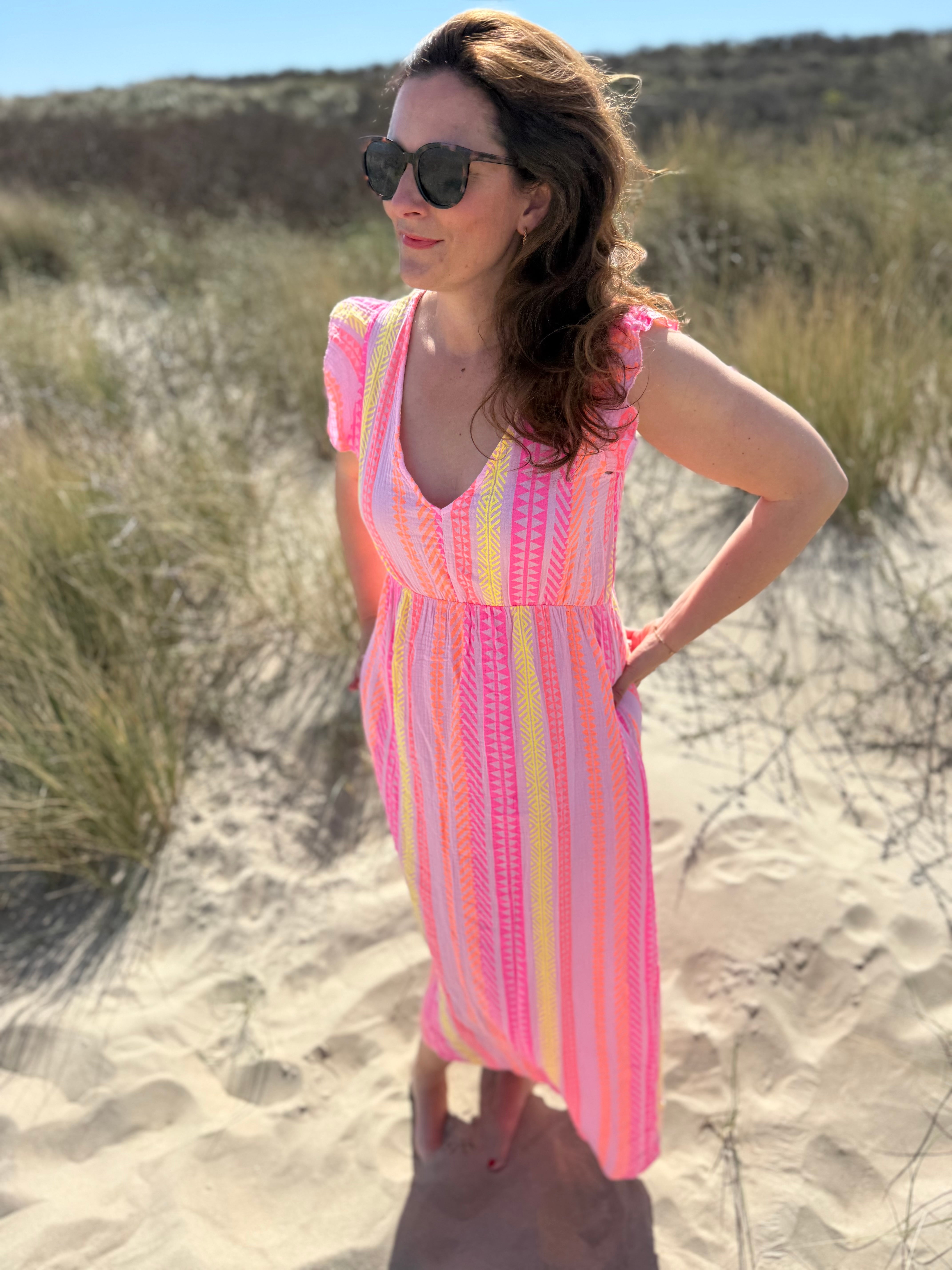 Musselinkleid in Maxilänge mit V Ausschnitt und kurzen Flügelärmeln. Das Kleid ist rosa mit pink, gelb und orangenen Ethno Muster.