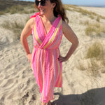 Musselinkleid in Midilänge mit V Ausschnitt. Es ist ärmellos und hat Schleifen an den Schultern zum binden. Das Kleid ist rosa mit pink, gelb und orangenen Ethno Muster.