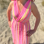 Musselinkleid in Midilänge mit V Ausschnitt. Es ist ärmellos und hat Schleifen an den Schultern zum binden. Das Kleid ist rosa mit pink, gelb und orangenen Ethno Muster.