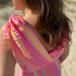 Musselinkleid in Midilänge mit V Ausschnitt. Es ist ärmellos und hat Schleifen an den Schultern zum binden. Das Kleid ist rosa mit pink, gelb und orangenen Ethno Muster.