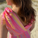 Musselinkleid in Midilänge mit V Ausschnitt. Es ist ärmellos und hat Schleifen an den Schultern zum binden. Das Kleid ist rosa mit pink, gelb und orangenen Ethno Muster.