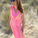 Musselinkleid in Midilänge mit V Ausschnitt. Es ist ärmellos und hat Schleifen an den Schultern zum binden. Das Kleid ist rosa mit pink, gelb und orangenen Ethno Muster.