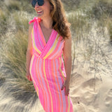 Musselinkleid in Midilänge mit V Ausschnitt. Es ist ärmellos und hat Schleifen an den Schultern zum binden. Das Kleid ist rosa mit pink, gelb und orangenen Ethno Muster.