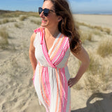 Musselinkleid in Midilänge mit V Ausschnitt. Es ist ärmellos und hat Schleifen an den Schultern zum binden. Das Kleid ist weiß mit pink und orangenen Ethno Muster.