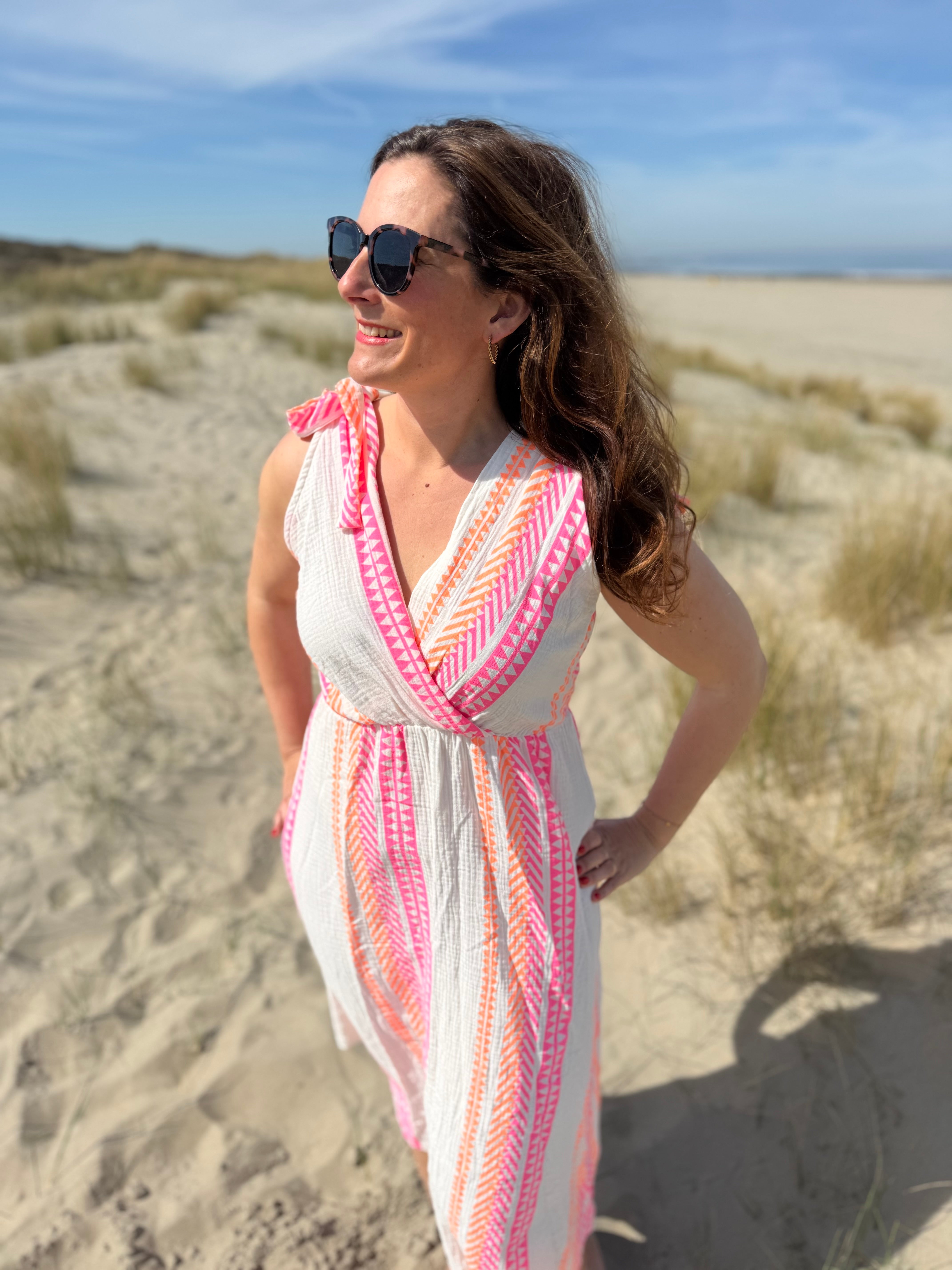 Musselinkleid in Midilänge mit V Ausschnitt. Es ist ärmellos und hat Schleifen an den Schultern zum binden. Das Kleid ist weiß mit pink und orangenen Ethno Muster.