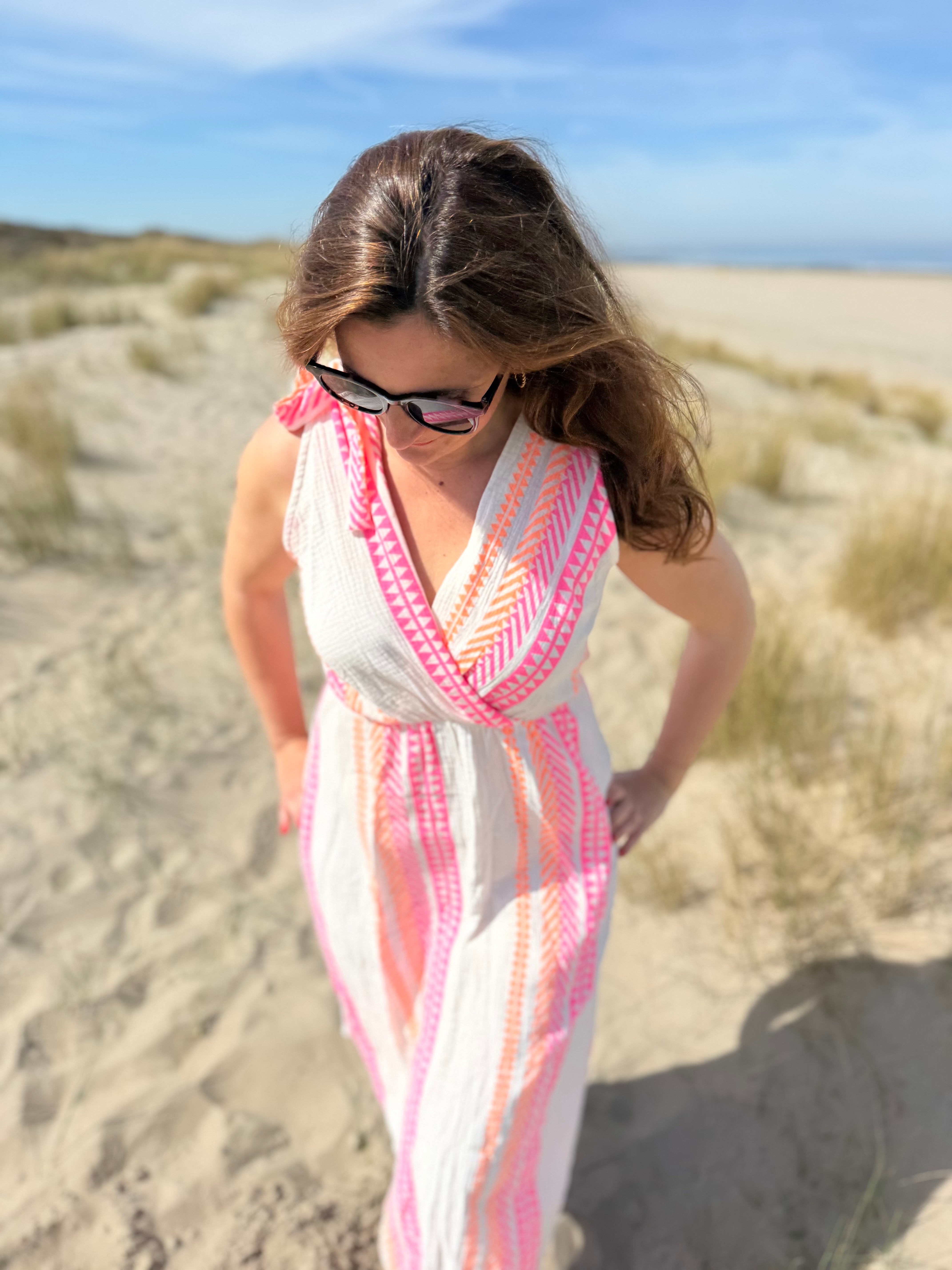 Musselinkleid in Midilänge mit V Ausschnitt. Es ist ärmellos und hat Schleifen an den Schultern zum binden. Das Kleid ist weiß mit pink und orangenen Ethno Muster.