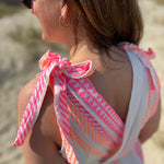 Musselinkleid in Midilänge mit V Ausschnitt. Es ist ärmellos und hat Schleifen an den Schultern zum binden. Das Kleid ist weiß mit pink und orangenen Ethno Muster.