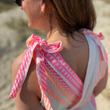 Musselinkleid in Midilänge mit V Ausschnitt. Es ist ärmellos und hat Schleifen an den Schultern zum binden. Das Kleid ist weiß mit pink und orangenen Ethno Muster.