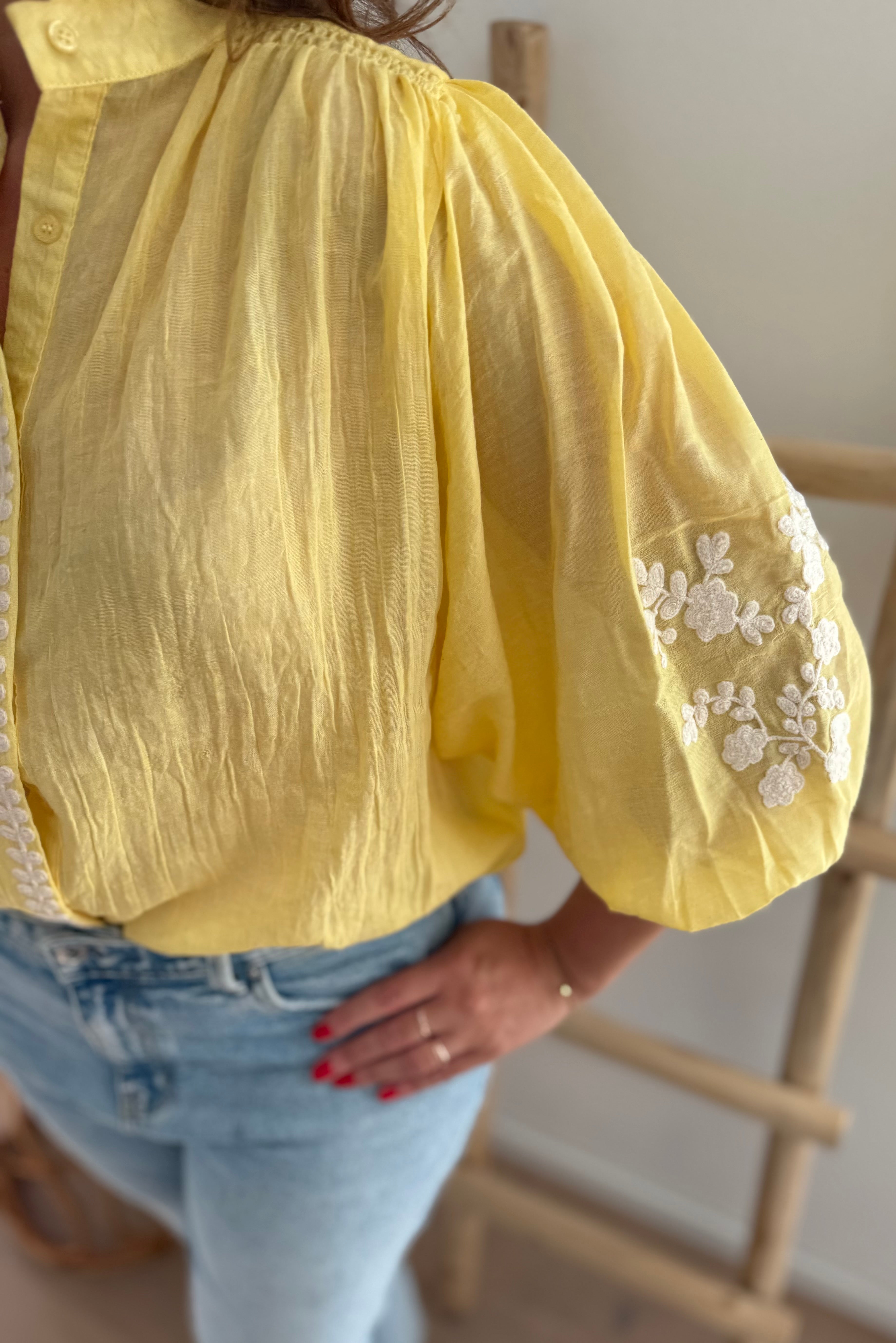 Leichte locker sitzende Baumwollbluse in gelb mit beigen Blumenstickereien an den Ärmeln.