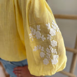 Leichte locker sitzende Baumwollbluse in gelb mit beigen Blumenstickereien an den Ärmeln.