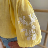 Leichte locker sitzende Baumwollbluse in gelb mit beigen Blumenstickereien an den Ärmeln.