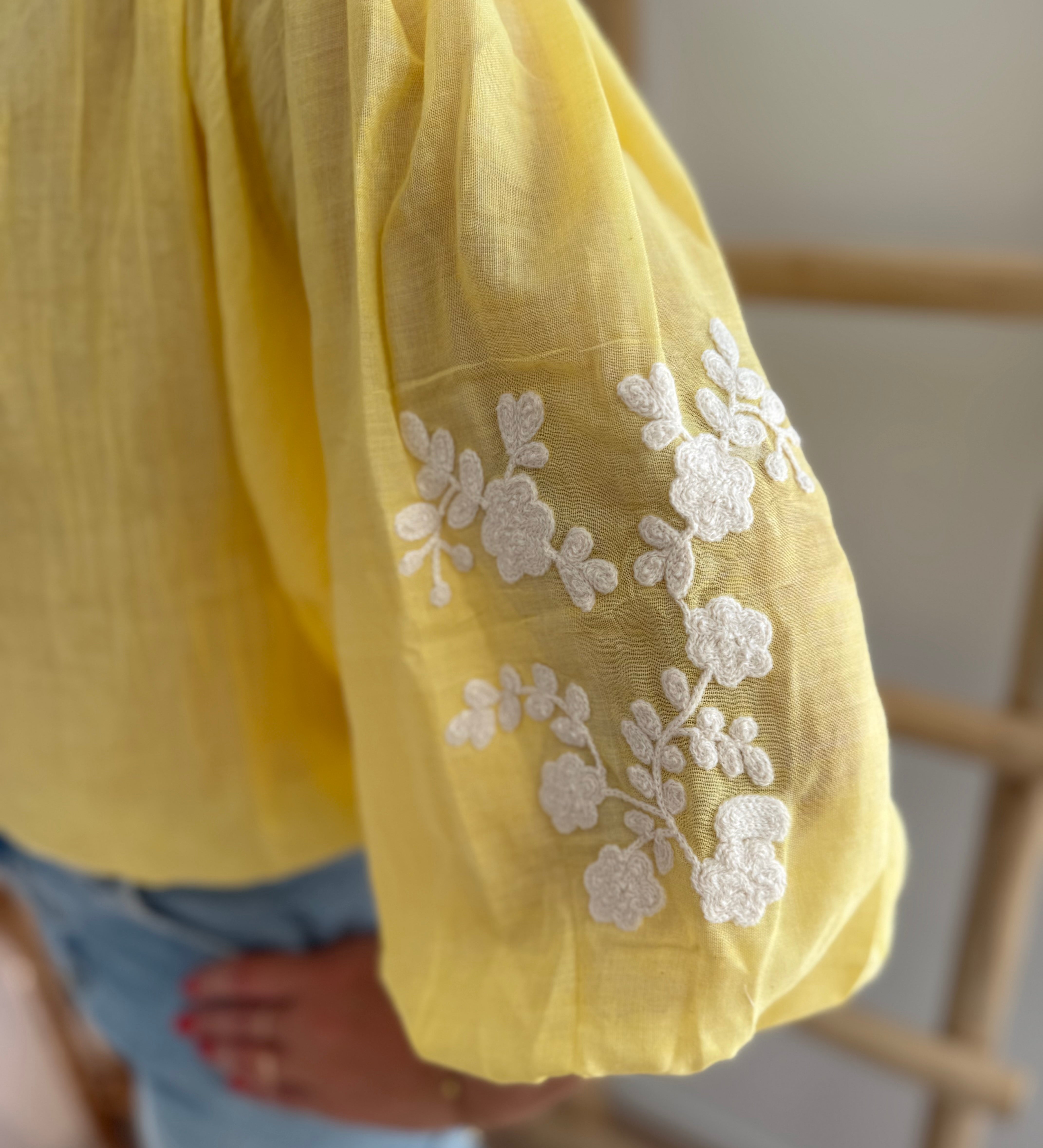 Leichte locker sitzende Baumwollbluse in gelb mit beigen Blumenstickereien an den Ärmeln.
