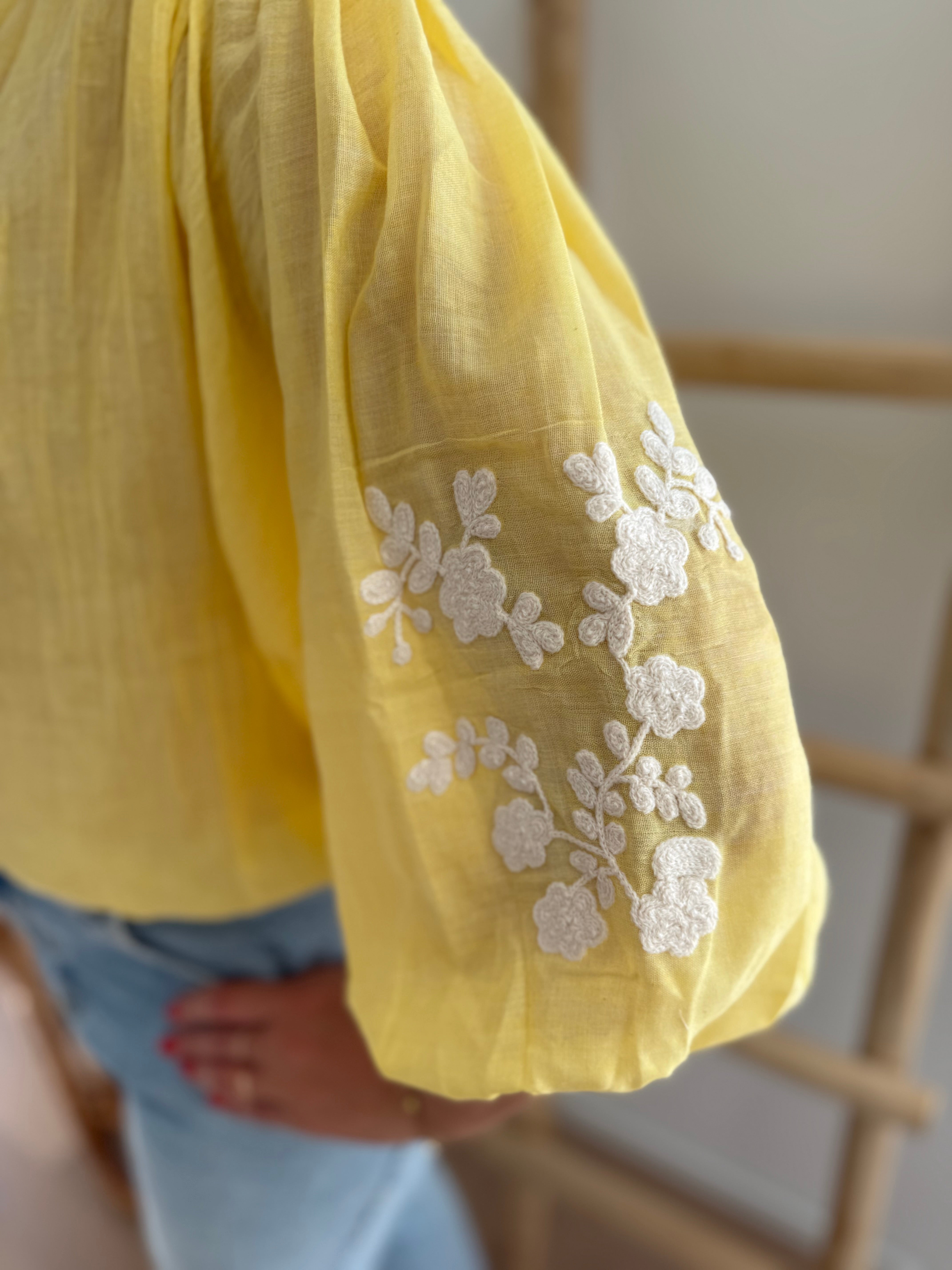 Leichte locker sitzende Baumwollbluse in gelb mit beigen Blumenstickereien an den Ärmeln.