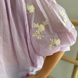 Leichte locker sitzende Baumwollbluse in flieder mit beigen Blumenstickereien an den Ärmeln.