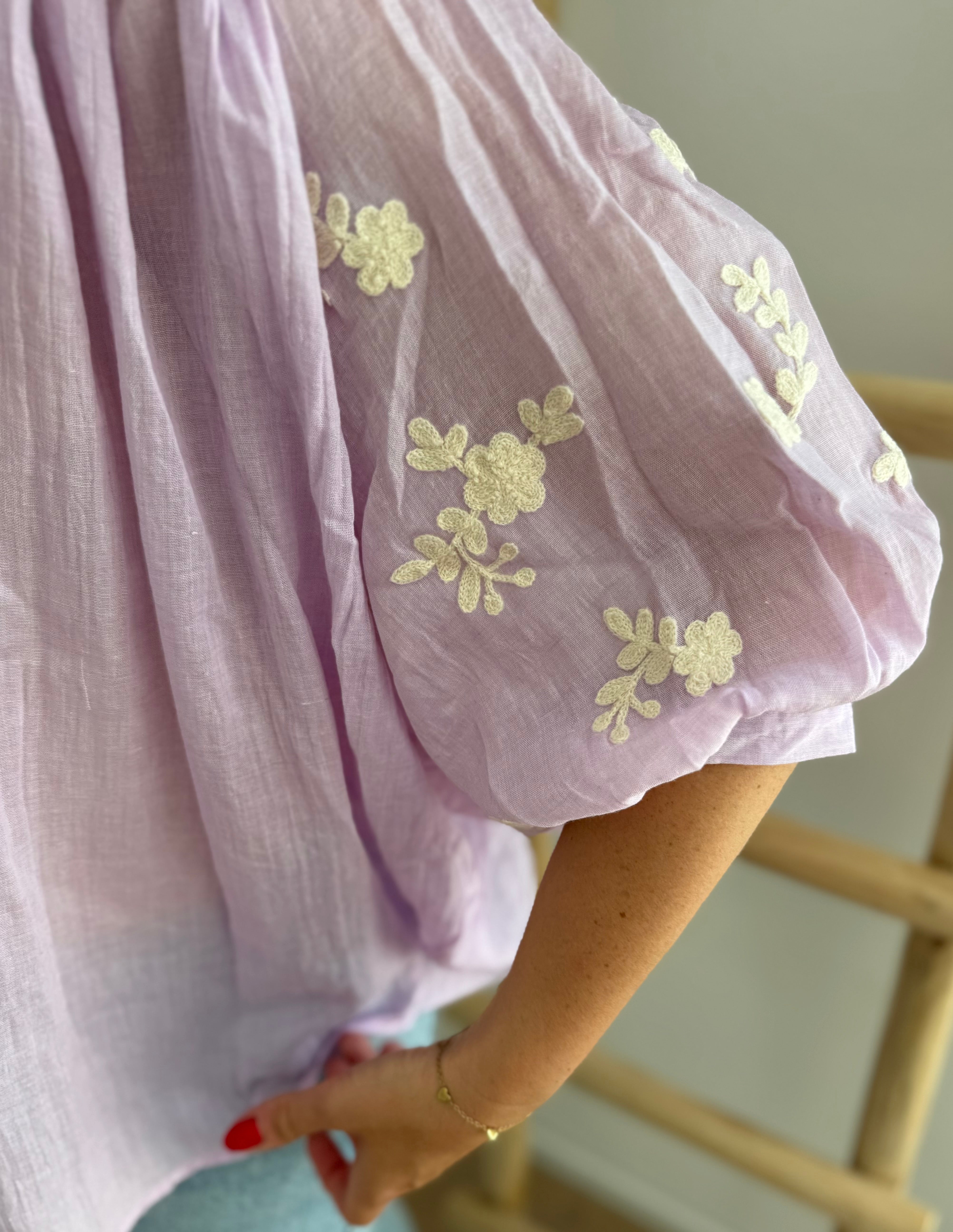 Leichte locker sitzende Baumwollbluse in flieder mit beigen Blumenstickereien an den Ärmeln.