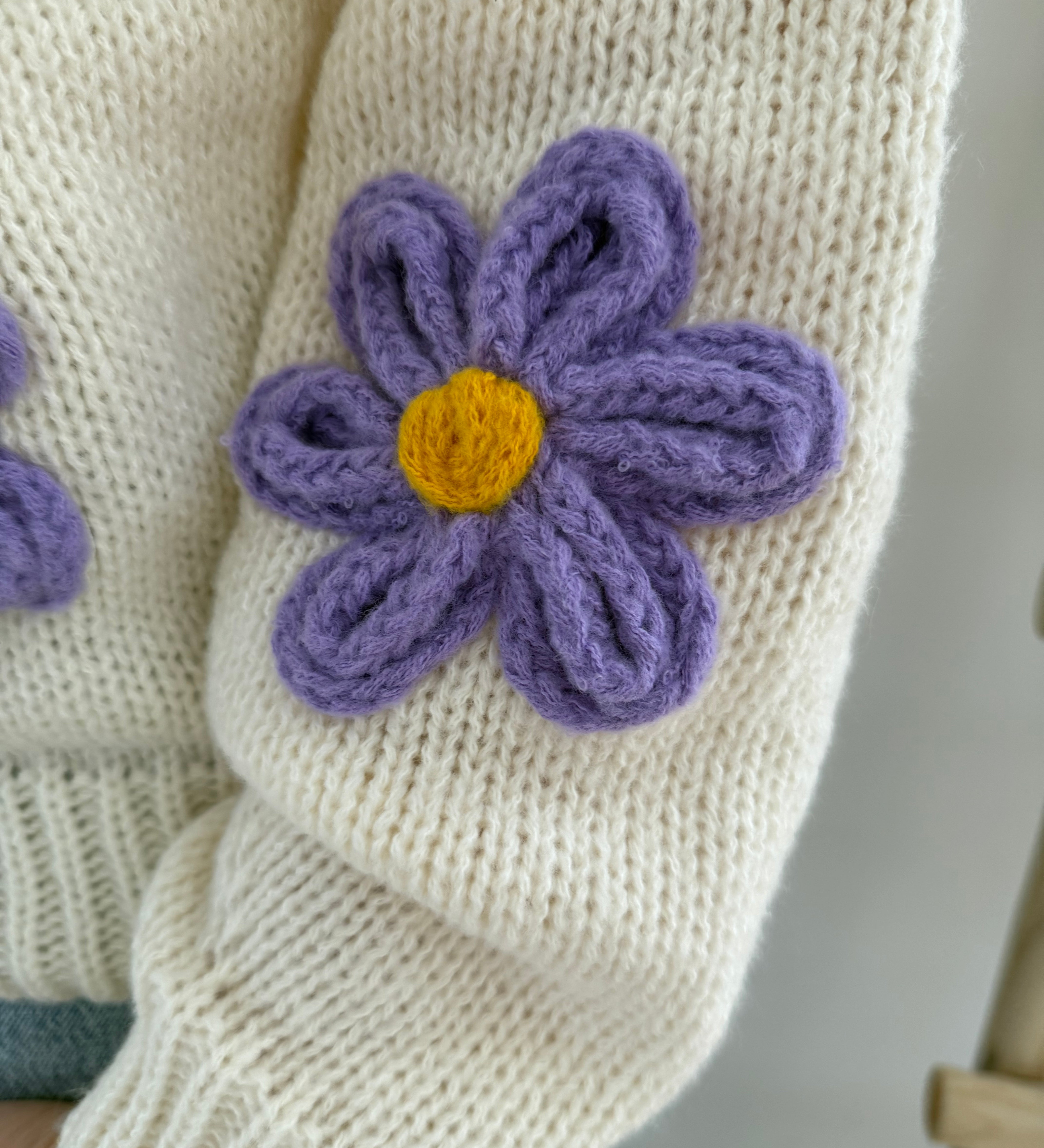 Statement Strickjacke in creme mit wunderschönen großen Blumenapplikationen in gelb und lila in Form einer Margerite . Die Strickjacke fällt locker und hat einen V Ausschnitt.